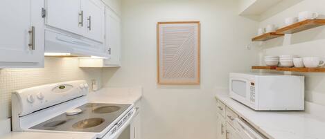 Una cocina compacta con armarios blancos, un microondas y una estufa.