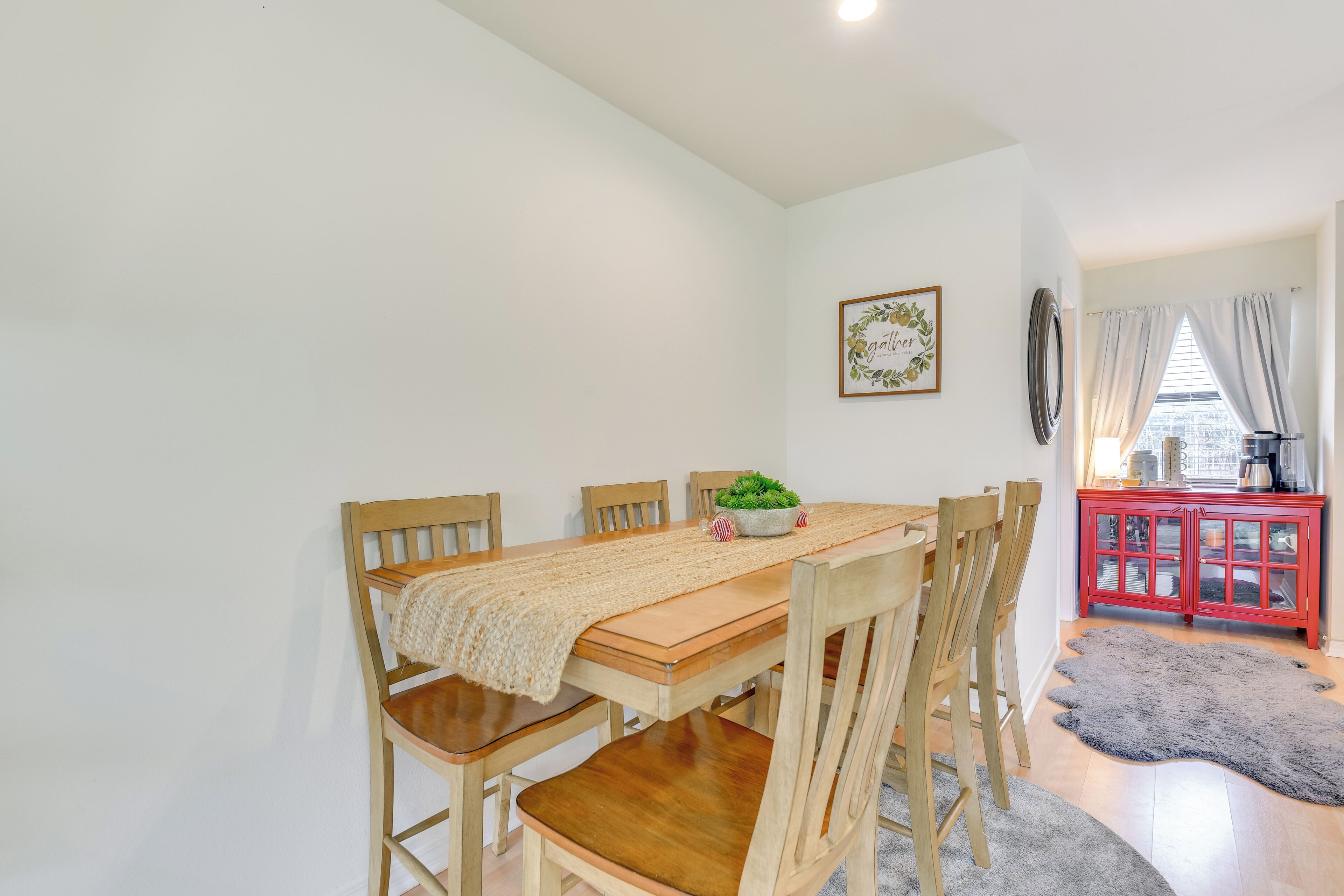 Un coin repas avec une table en bois, des chaises, un chemin de table en tissu tissé, une plante en pot et un buffet rouge aux portes en verre.