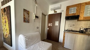 Una stanza con un divano bianco, una cucina con mobili in legno e un grande quadro appeso al muro.