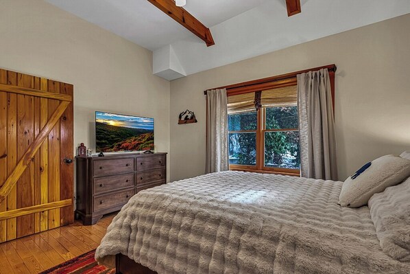 A bedroom with a large bed, wooden wardrobe, and a window with curtains.