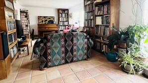 Een woonkamer met een gestreept bankje, een houten boekenkast en een potplant.