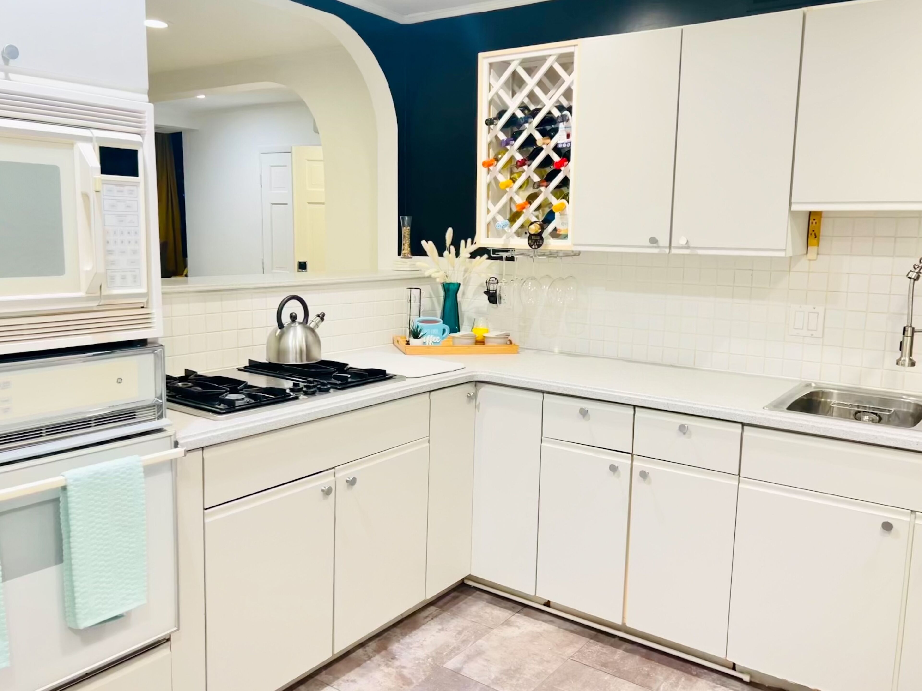 A modern kitchen with white cabinets, a stainless steel kettle, a microwave, and a wine rack.