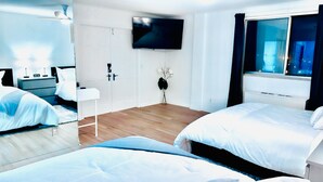 Une chambre d’hôtel avec deux lits, un téléviseur fixé au mur, une table de chevet, une armoire et une fenêtre avec des rideaux.