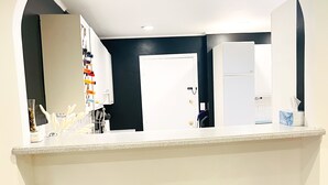 Une cuisine avec un comptoir blanc, deux tabourets de bar et une porte donnant sur une autre pièce.