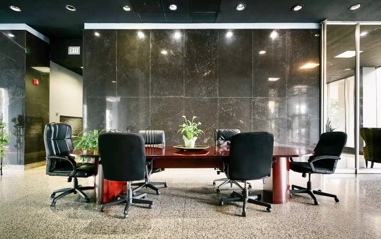 A conference room with a dark marble wall, a wooden table, and four black office chairs.