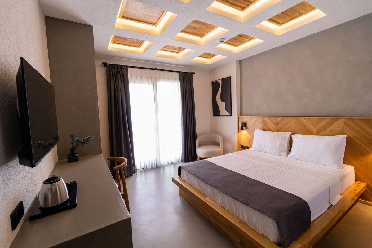Une chambre d’hôtel moderne dotée d’un grand lit, d’une télévision à écran plat, d’un bureau avec une machine à café et d’une chaise.