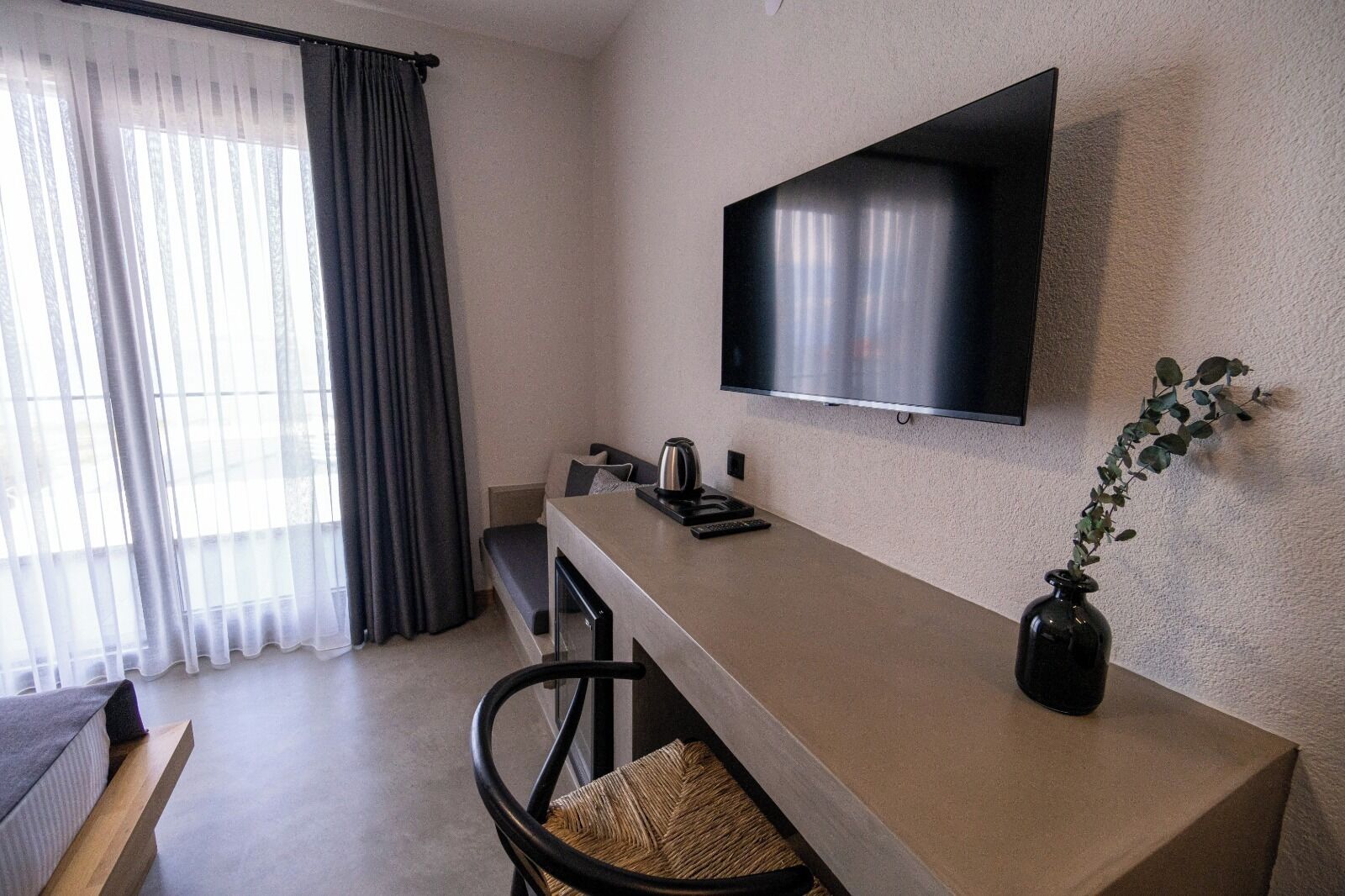 Ein modernes Zimmer mit einem wandmontierten Flachbildfernseher, einem kleinen Tisch mit Fernbedienung, einem Sessel und einem Blumentopf.
