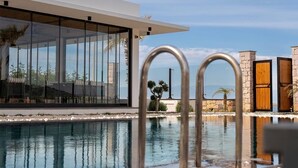 A modern pool area with clear glass walls, a stone structure, and a view of the sea. - Leone Cunda Edition Otel (Ayvalik)