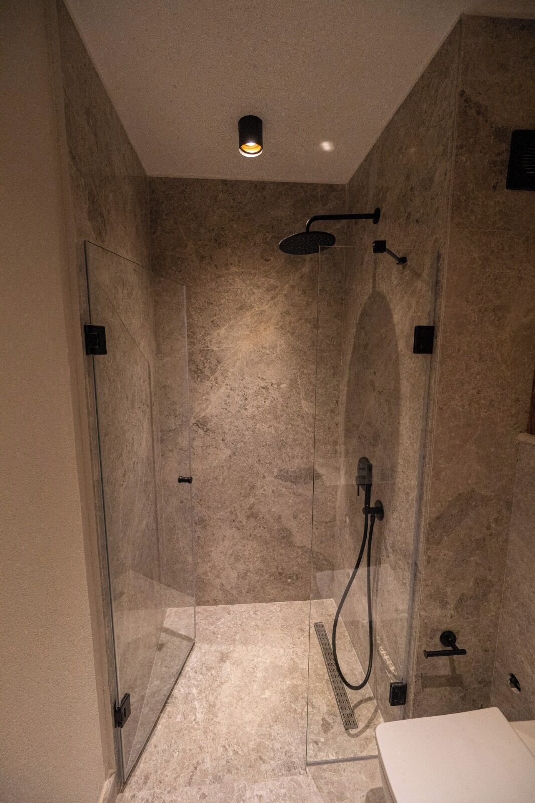 Una ducha moderna con cabina de vidrio, cabezal de ducha de mano y panel de control en la pared.