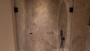 Una ducha moderna con cabina de vidrio, cabezal de ducha de mano y panel de control en la pared.