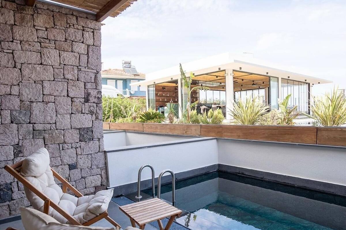 Un espace piscine aménagé sur le toit, avec un mur en pierre, une terrasse en bois et un bâtiment moderne en arrière-plan.