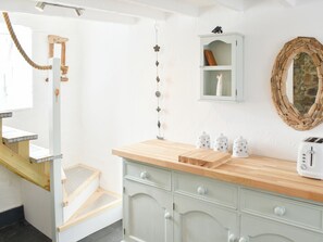 A kitchen with a wooden countertop, a white cabinet, a stone wall, and a wooden staircase.