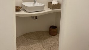 Un baño con un lavamanos blanco, un espejo redondo y una pequeña cesta de mimbre.