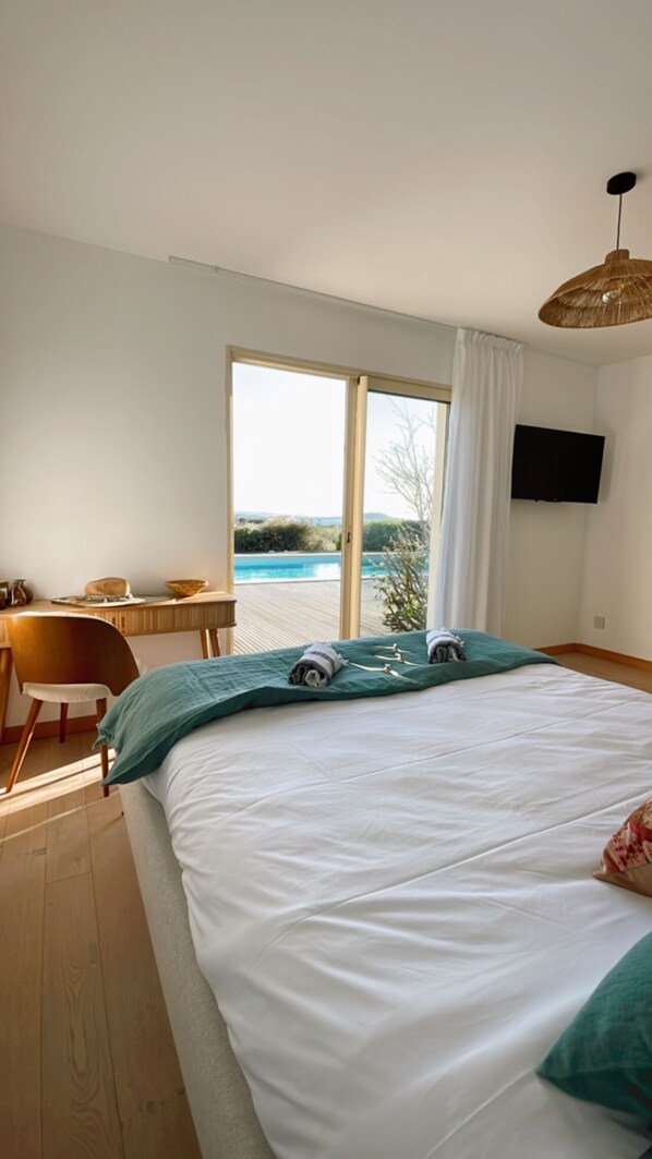 A bedroom with a large bed, a desk, and a view of a swimming pool.