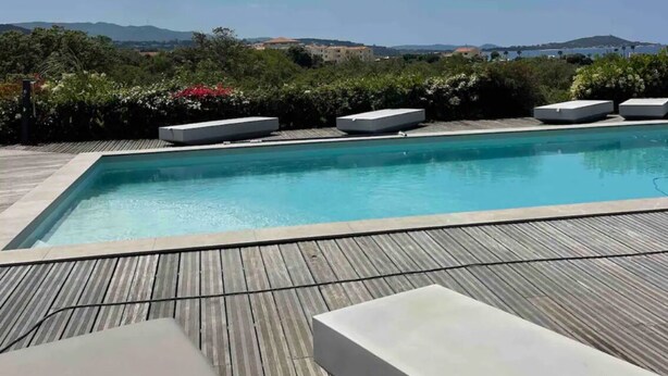 Una piscina con cubierta de madera, sillas de descanso y vistas al paisaje.