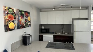 Cocina moderna con armarios blancos, pileta de acero inoxidable, microondas integrado y horno doble. Hay un bote de basura negro y un pequeño electrodoméstico negro en la encimera.