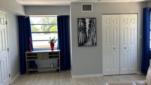 Una habitación con ventana, escritorio, puerta y una obra de arte colgada en la pared.