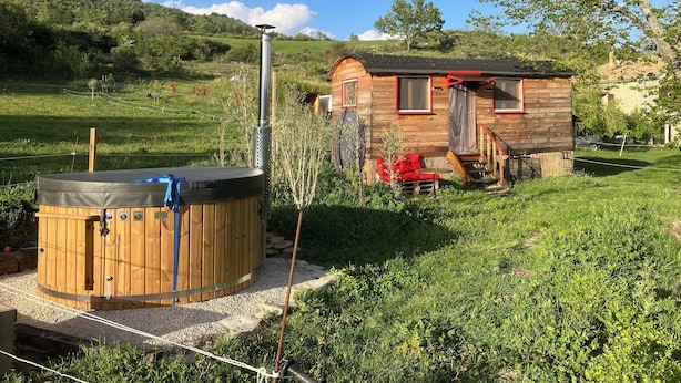 Une cabane en bois dotée d’un bain à remous et d’une petite terrasse, entourée de verdure et avec une montagne en toile de fond.