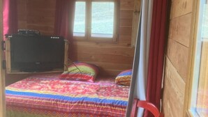 Une chambre dans un chalet en bois, comprenant deux lits, une table, une chaise, un téléviseur et une fenêtre avec des rideaux.