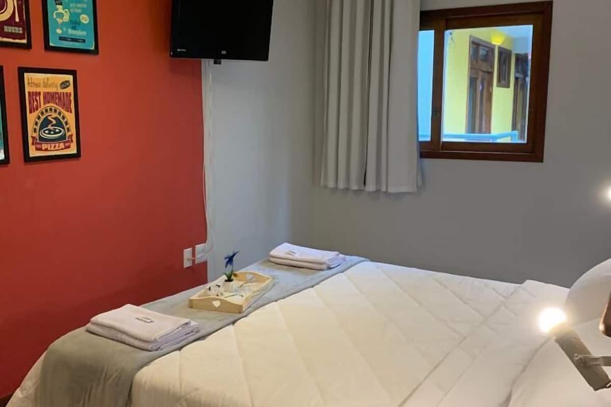 Une chambre d’hôtel avec un lit, un téléviseur à écran plat, une fenêtre avec des rideaux et un mur orné de tableaux.