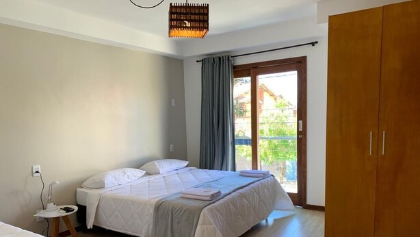 A bedroom with a bed, a nightstand, a wardrobe, and a window with curtains. - POUSADA LAZULI (Macaé)