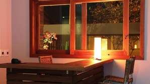 A wooden dining table with a chair, a window with a wooden frame, and a vase with flowers. - POUSADA LAZULI (Macaé)