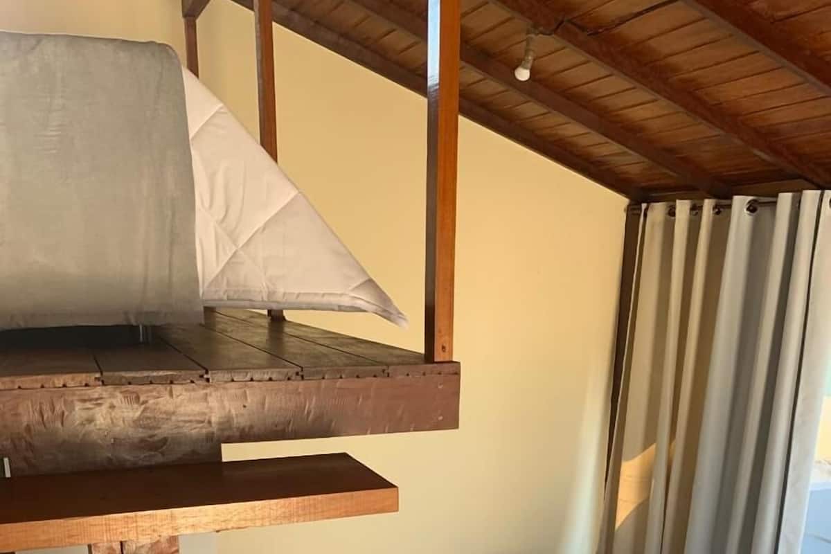 Une chambre avec un lit en mezzanine, une petite table de chevet et une fenêtre avec des rideaux.