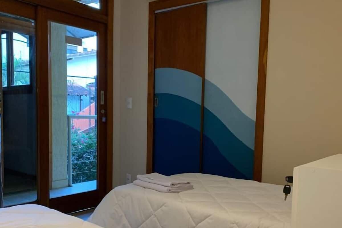 Une chambre d’hôtel avec deux lits, une porte-fenêtre coulissante donnant sur l’extérieur et un climatiseur fixé au mur.