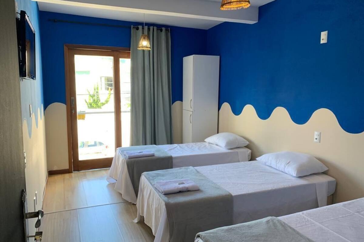 Une chambre d’hôtel avec deux lits simples, une armoire et une vue sur l’extérieur, visible à travers une porte vitrée.