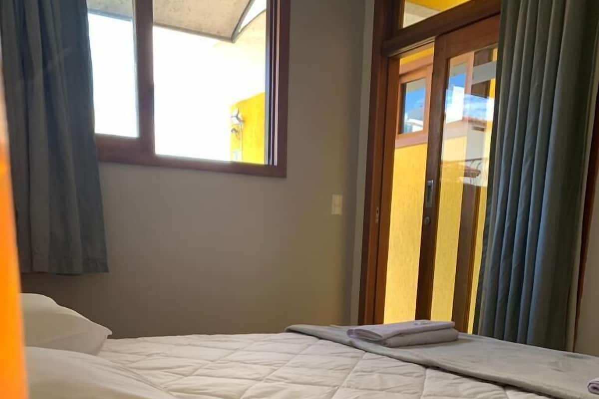 Un lit bien fait, recouvert d’une courtepointe matelassée, une fenêtre avec des rideaux et une vue sur l’extérieur.