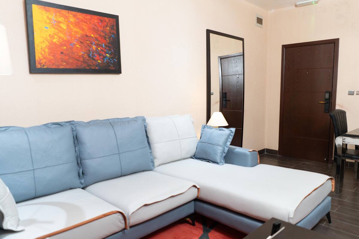 A modern living room with a sectional sofa, a dining table, and a door.