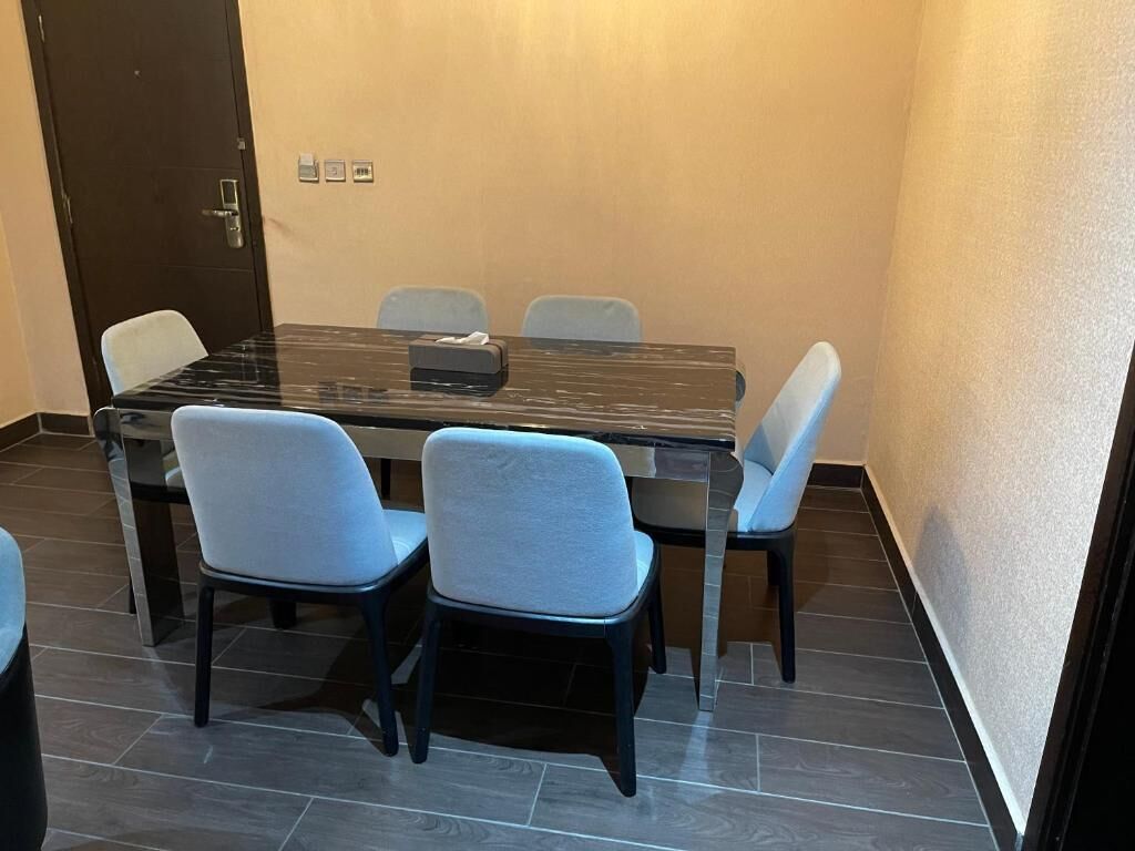 A conference room with a black marble table, six light grey chairs, and a dark door.