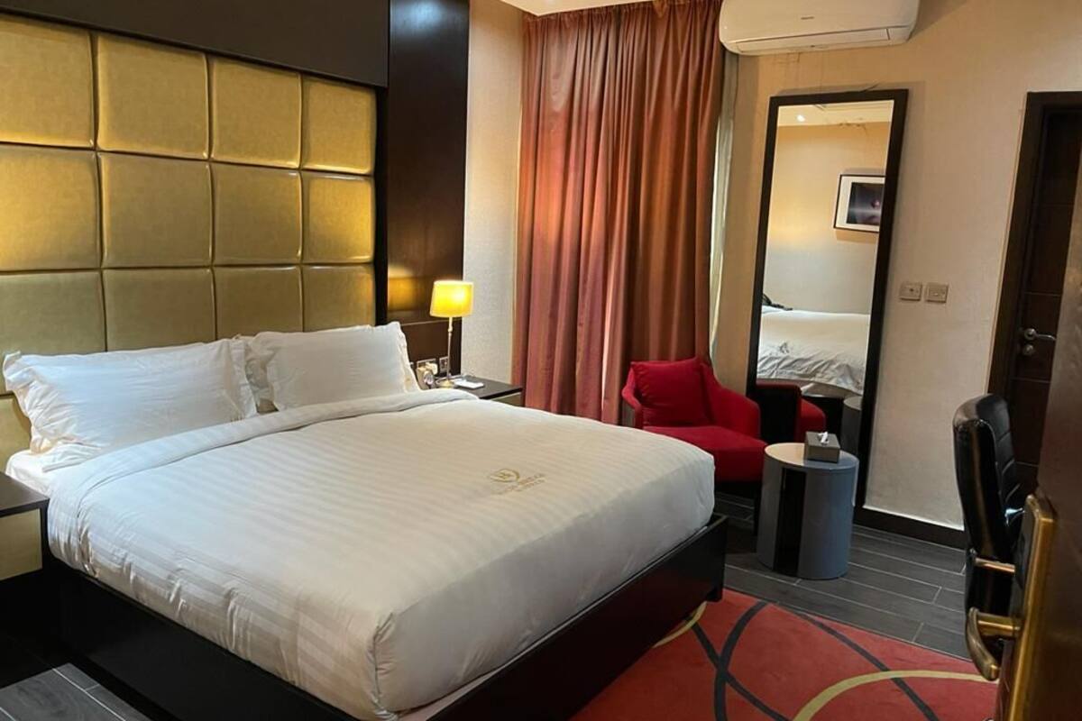 A hotel room with a large bed, a red chair, a small table, and a mirror.