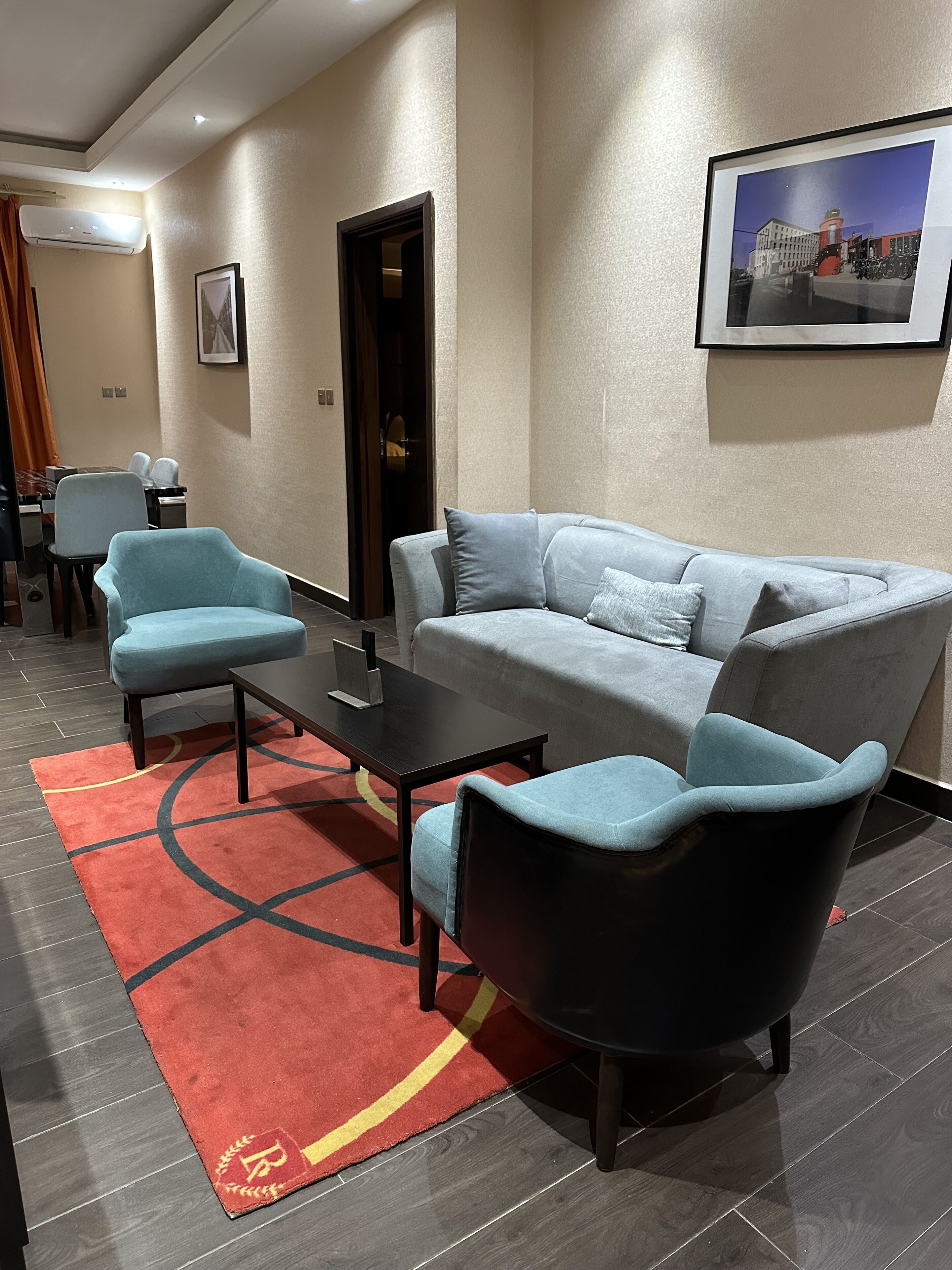 A modern hotel lobby with a grey sofa, two armchairs, a coffee table, and a red rug.