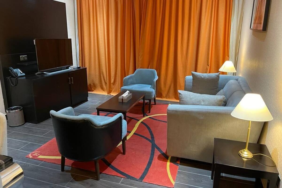 A hotel room with a sofa, two armchairs, a coffee table, a TV, a desk, and a lamp.