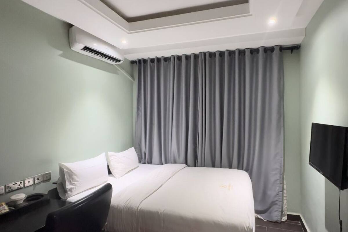 A hotel room with a bed, a desk, a flat-screen TV, and an air conditioning unit.