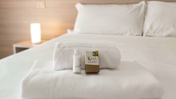 Una cama bien hecha, con una toalla blanca, un frasco de producto para el cuidado de la piel y una caja de producto con un logotipo de hoja verde.