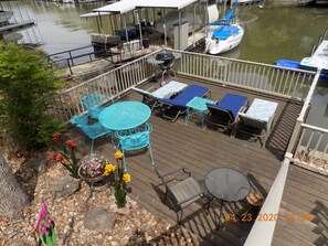 Eine Holzterrasse mit Gartenmöbeln, ein kleiner Garten mit Blumen und Blick auf Wasser und Boote.