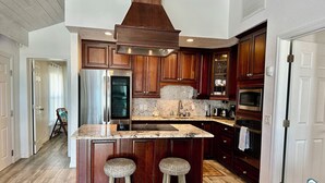 Eine moderne Küche mit dunklen Holzausziehtüren, einem Edelstahl-Kühlschrank, einem eingebauten Backofen und einer Arbeitsplatte aus Granit.