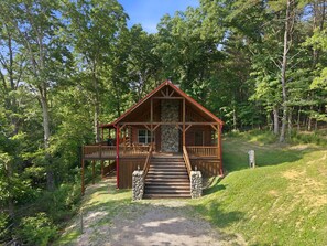 A log cabin with a porch, stone foundation, and a staircase leading to the entrance. - Double Down Lodge | 5BR Group Getaway, Hot Tub & Game Room Near Old Man's Cave (Logan)