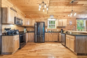Interior de una cabaña de madera con cocina, que incluye un refrigerador de acero inoxidable, armarios de madera y una encimera negra.