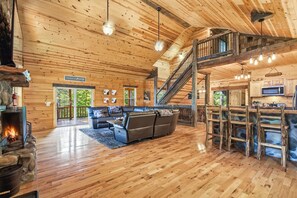 A spacious living area with a fireplace, a staircase, and a kitchen area. - Double Down Lodge | 5BR Group Getaway, Hot Tub & Game Room Near Old Man's Cave (Logan)