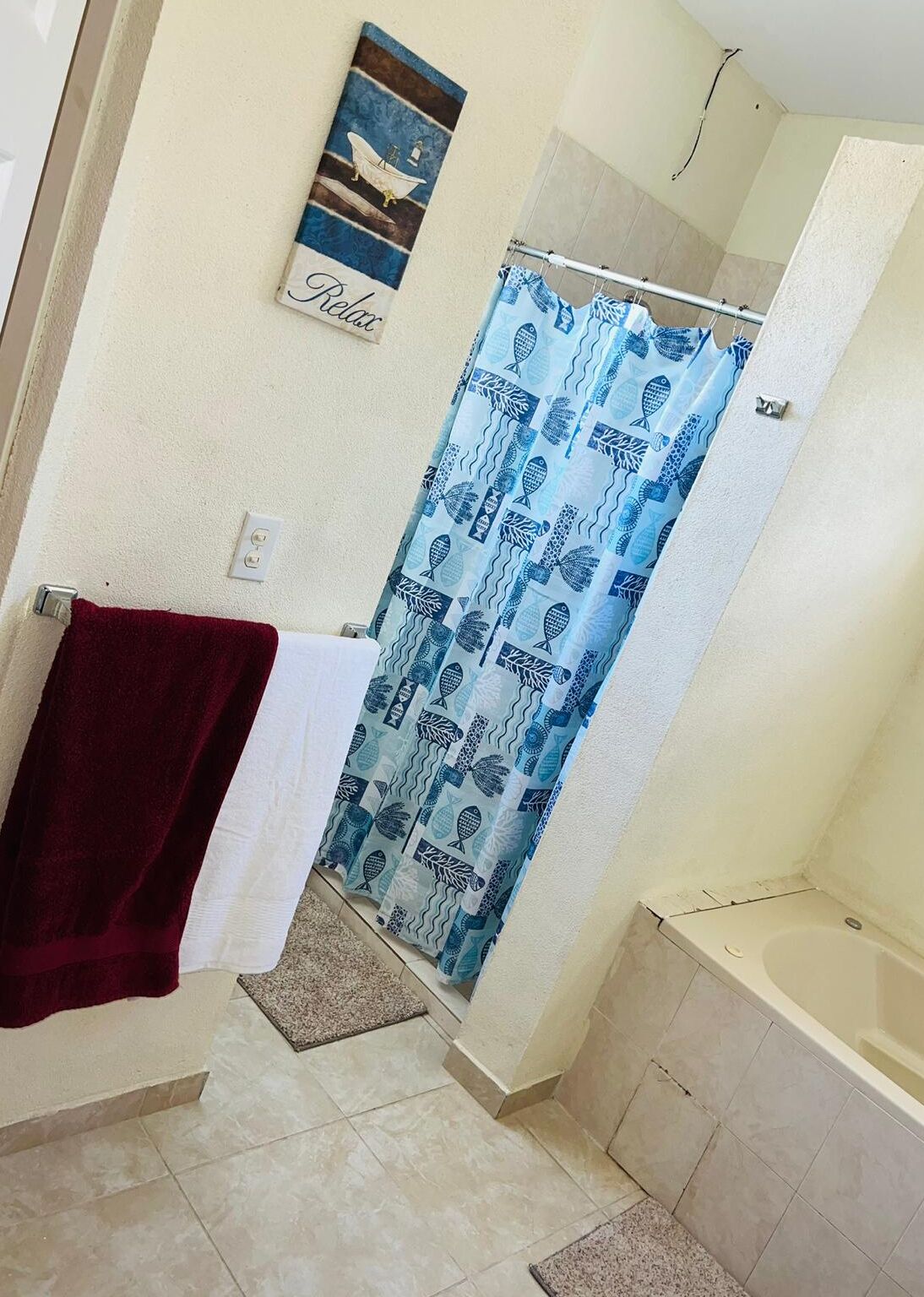 A bathroom with a shower curtain featuring a fish pattern, a towel rack with a red towel, and a framed picture on the wall.