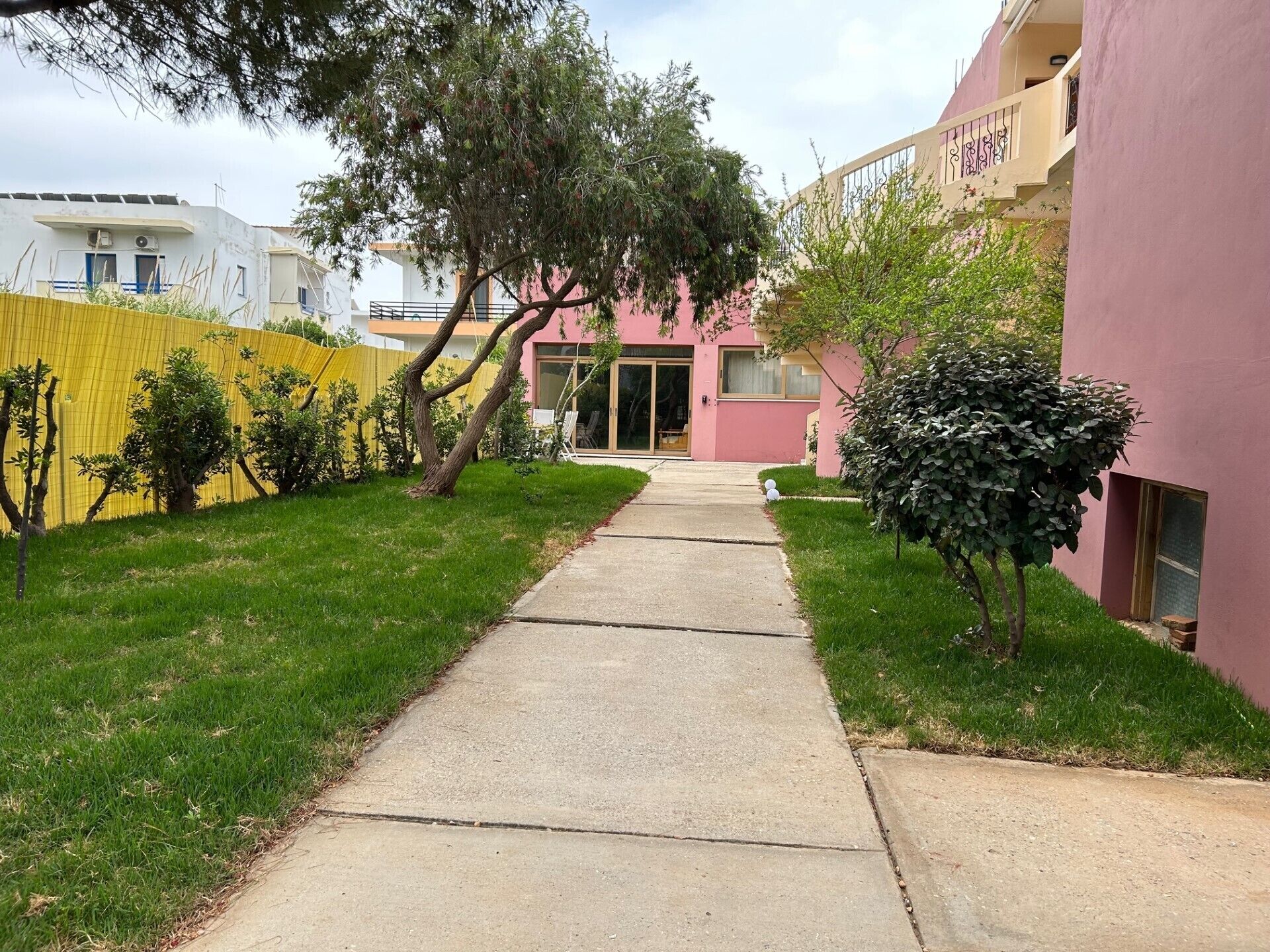 A pathway leading to a building with a pink facade and a yellow fence.