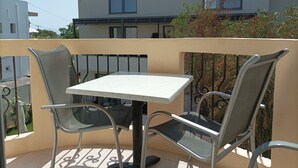 A balcony with a table and two chairs, a view of a building, and a railing. - Mediterranean Sea Top Floor (Kantanos-Selino)