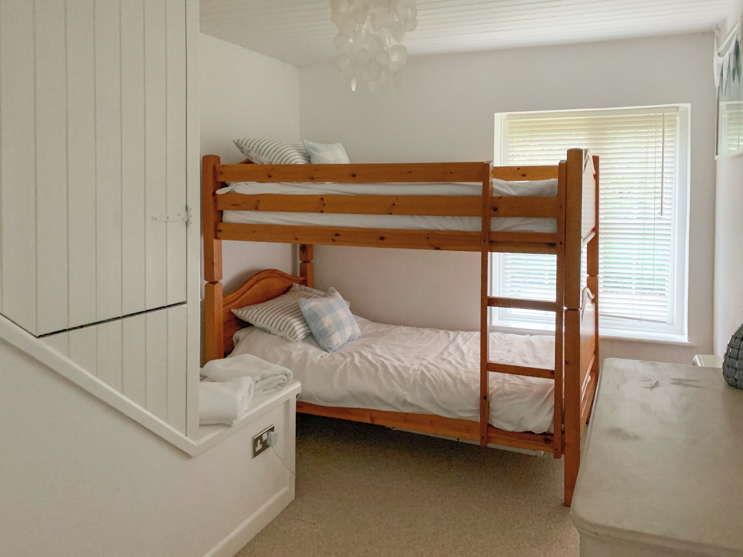 A bunk bed room with a wooden frame, white bedding, and a window with blinds.