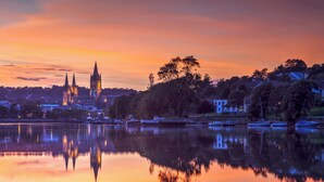 A calm lake with a church and residential buildings in the background.