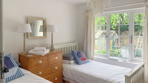 A bedroom with two single beds, a wooden dresser, a mirror, and a window with a view of the garden.