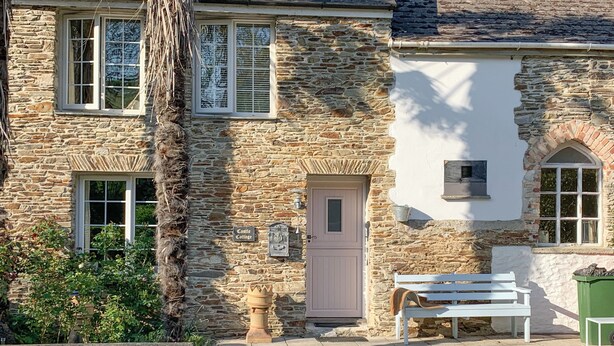 A stone cottage with a white door, a bench outside, and a sign reading "Castle Cottage".