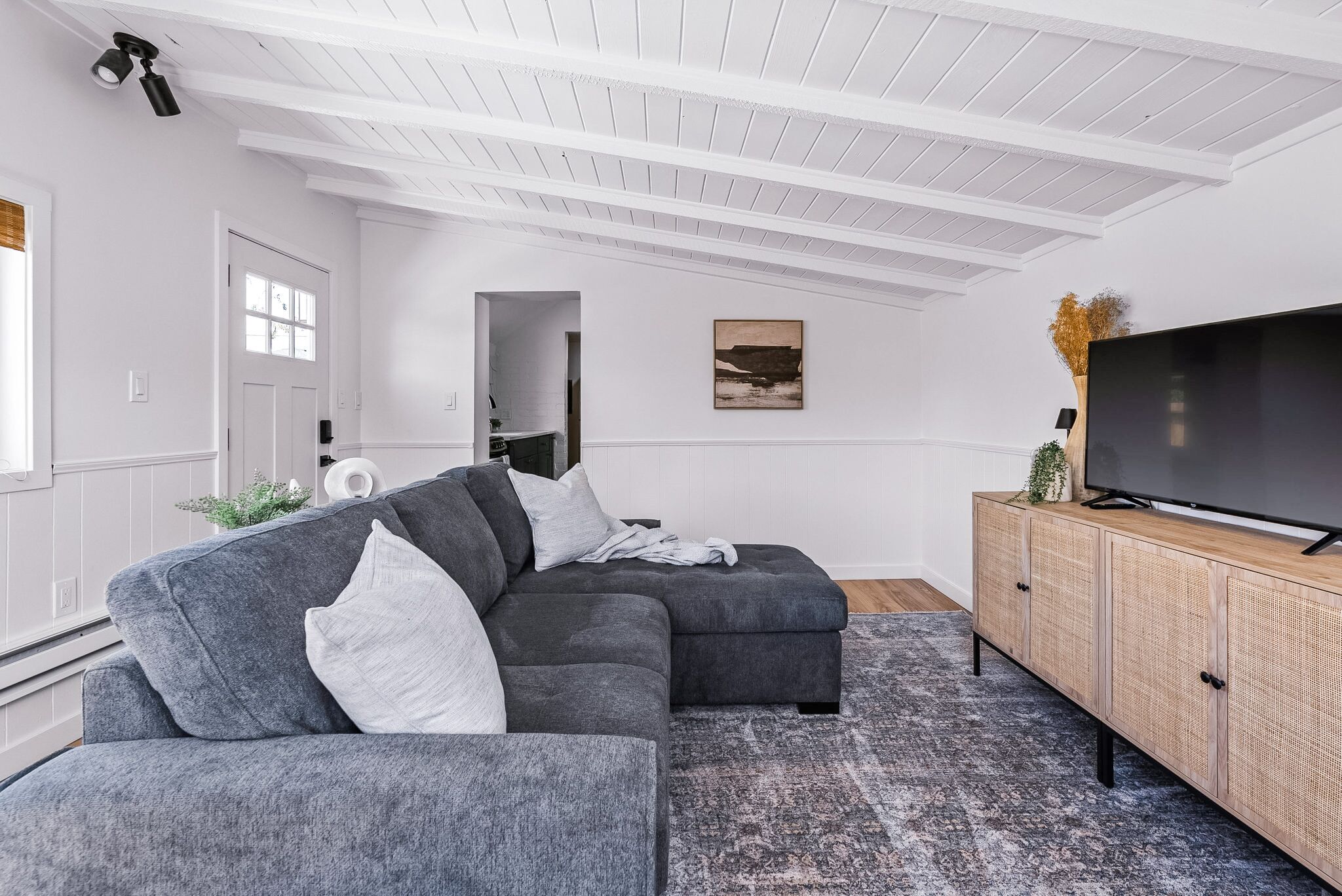 Een moderne woonkamer met een grijze modulaire bank, een flatscreen televisie op een houten kast en een kamerkleed met dessin.